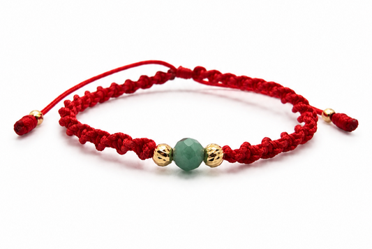 18K solid gold raw emerald bracelet with two diamond-cut gold beads on a red spiral macramé cord, close-up on white background